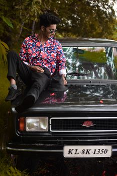 Stylish man posing on a vintage car in an outdoor setting, showcasing fashion and style.