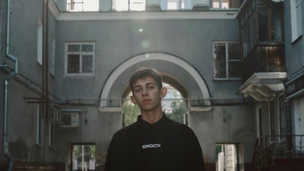 Young male in casual clothes looking at camera while standing near old gray building in daytime