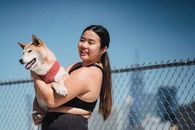 阳光明媚的户外，一位年轻女子快乐地抱着一只柴犬