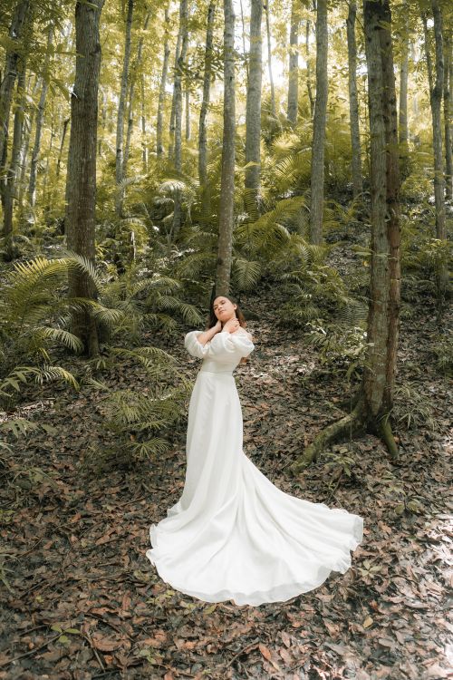 Free From above of young stylish woman in white bridal dress touching neck in woods in summer Stock Photo