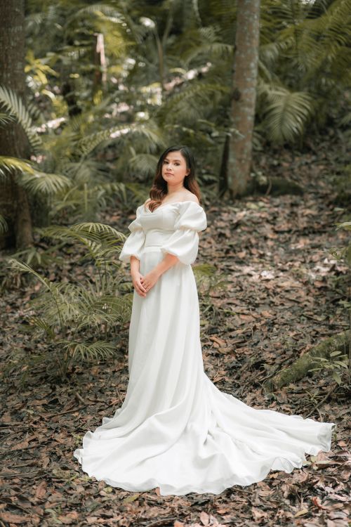 Free Young contemplative ethnic female in stylish bridal dress standing near fern plants while looking at camera Stock Photo
