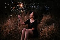 夜晚，一位微笑的女子在户外草地上欣赏烟花，流露出纯粹的喜悦