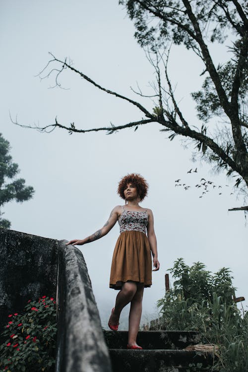 Woman Wearing Red and Black Spaghetti Strap Dress Holding Concrete Railings Under Bare Tree