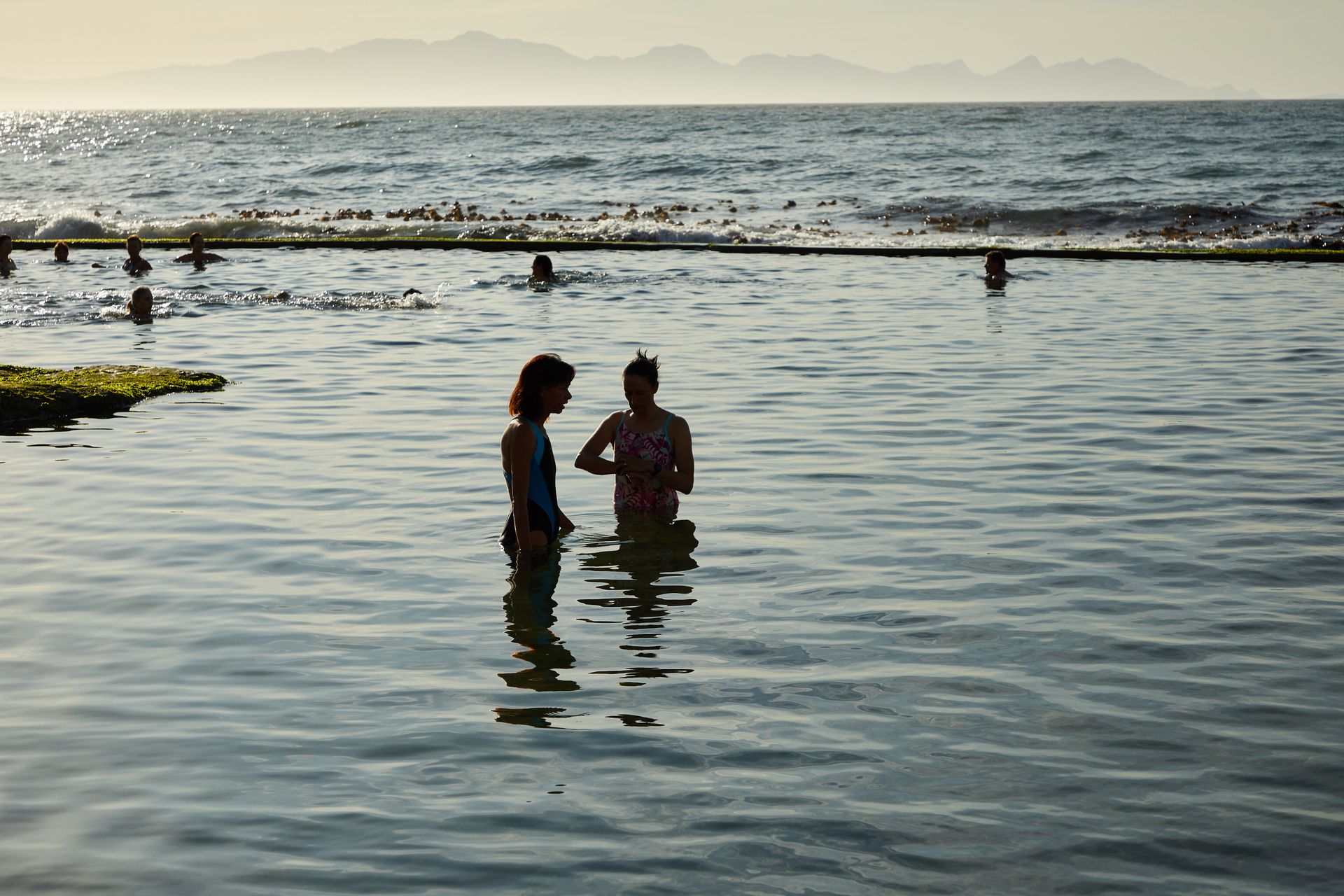 People wade through shallow waters during a picturesque beach sunset, capturing serene coastal beauty.