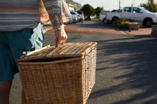 Free Casual outdoor scene with a person carrying a picnic basket in a sunny parking area. Stock Photo