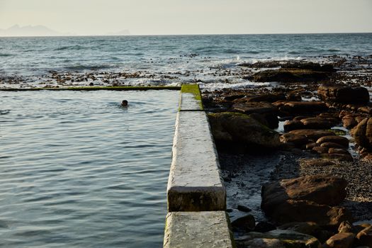 Person Swimming on Tidal Pool Beside a Rocky Seashore