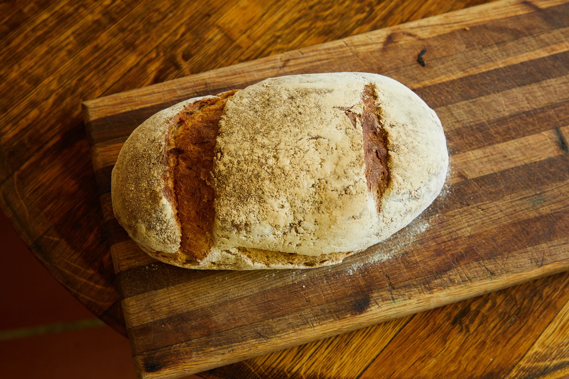 a rustic golden sourdough loaf fresh from the oven, crust dusted with flour, resting on a wooden cou