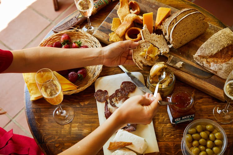 A Person Holding A Bread And A Spoon With Dip Near The Table With Food