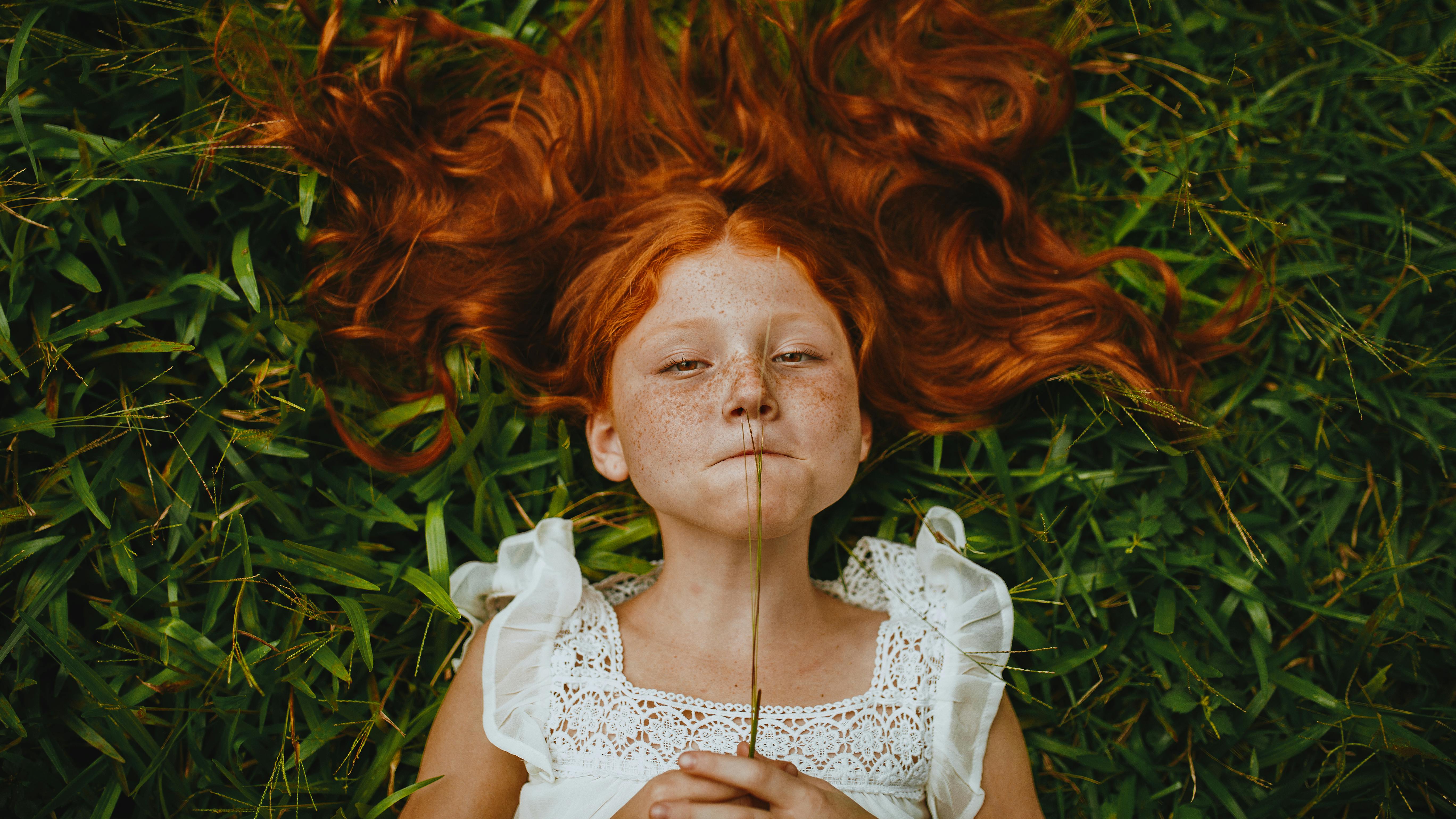 girl holding plant while lying on grass