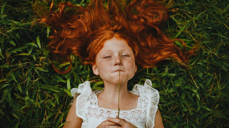 Girl Holding Plant While Lying On Grass