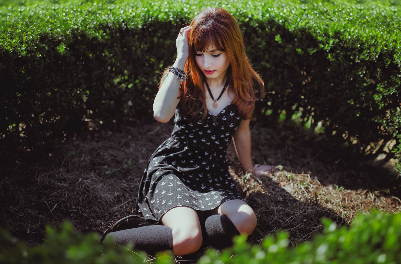 portrait of a young woman with red hair in a black dress sitting outdo