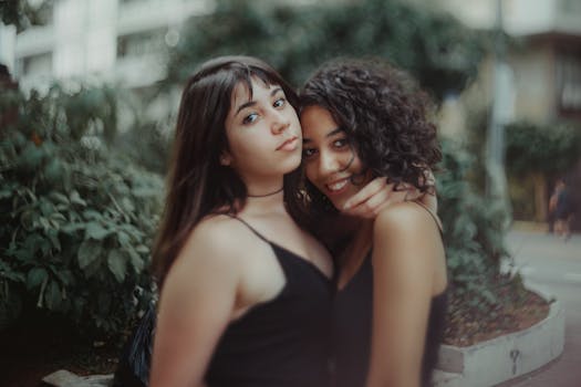 Two young women posing closely and smiling in an outdoor setting.