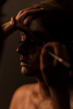 Close-up portrait of a woman with artistic makeup, set against a dark background.
