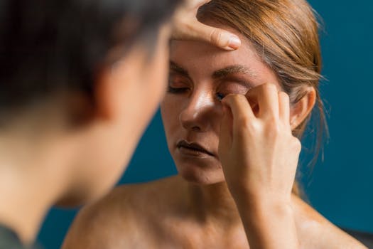 Close-up of a woman receiving artistic makeup indoors, showcasing creative beauty techniques.