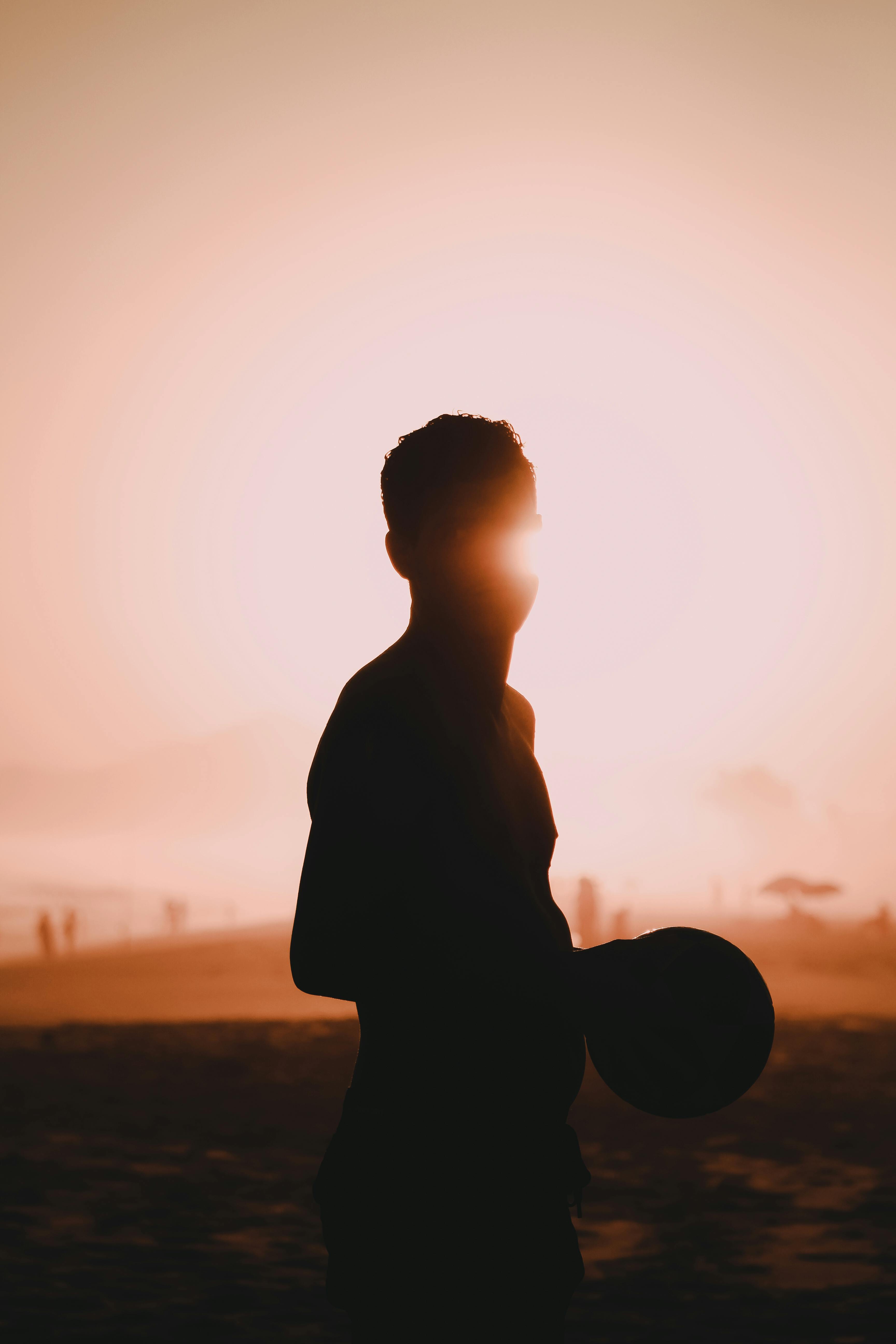 A silhouette of a man holding a ball on a beach at sunset, creating a dramatic and moody scene.