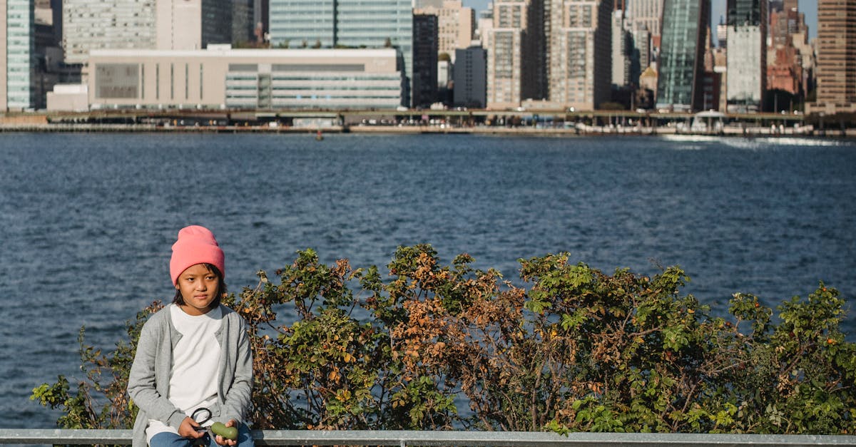 Full body of ethnic child sitting on metal fence and holding leash with puppy while spending time together