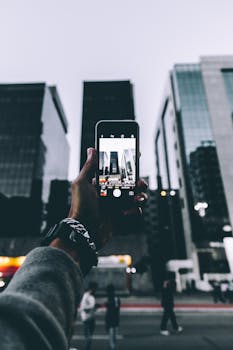 一部智能手机捕捉了城市中摩天大楼的景观，前景的人物显得模糊