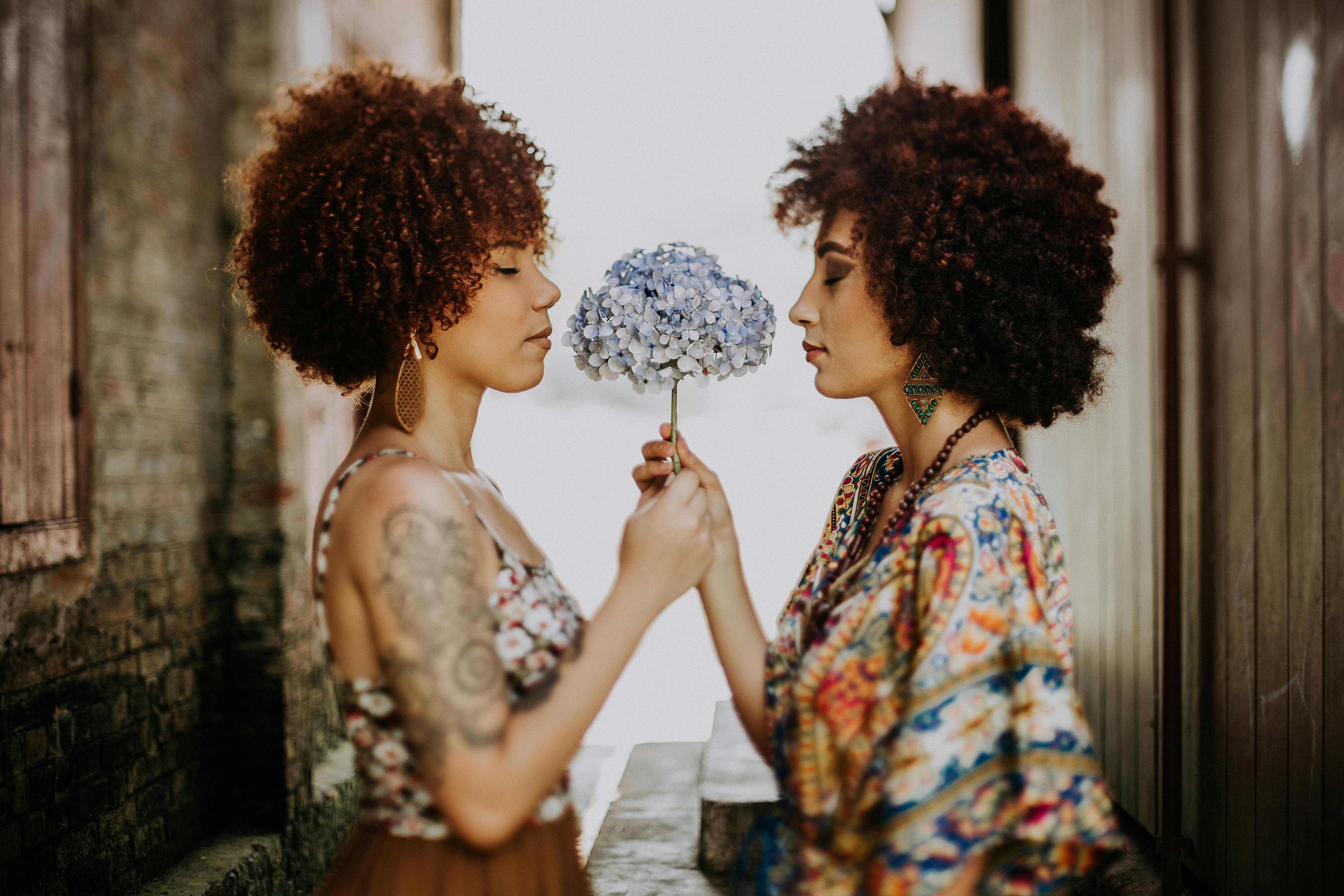 two women facing each other holding white and blue petaled flower