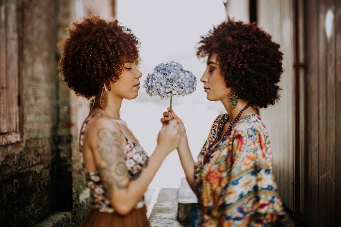 Two Women Facing Each Other Holding White-and-blue Petaled Flower