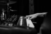 Black and white of crop anonymous tattooed musician playing chord on synthesizer with sound board