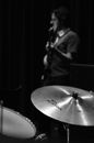 Black and white side view of male musician playing guitar against drum and cymbals during musical performance on black background