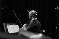 Black and white back view of male musician in earphone with violoncello and bow against musical notation
