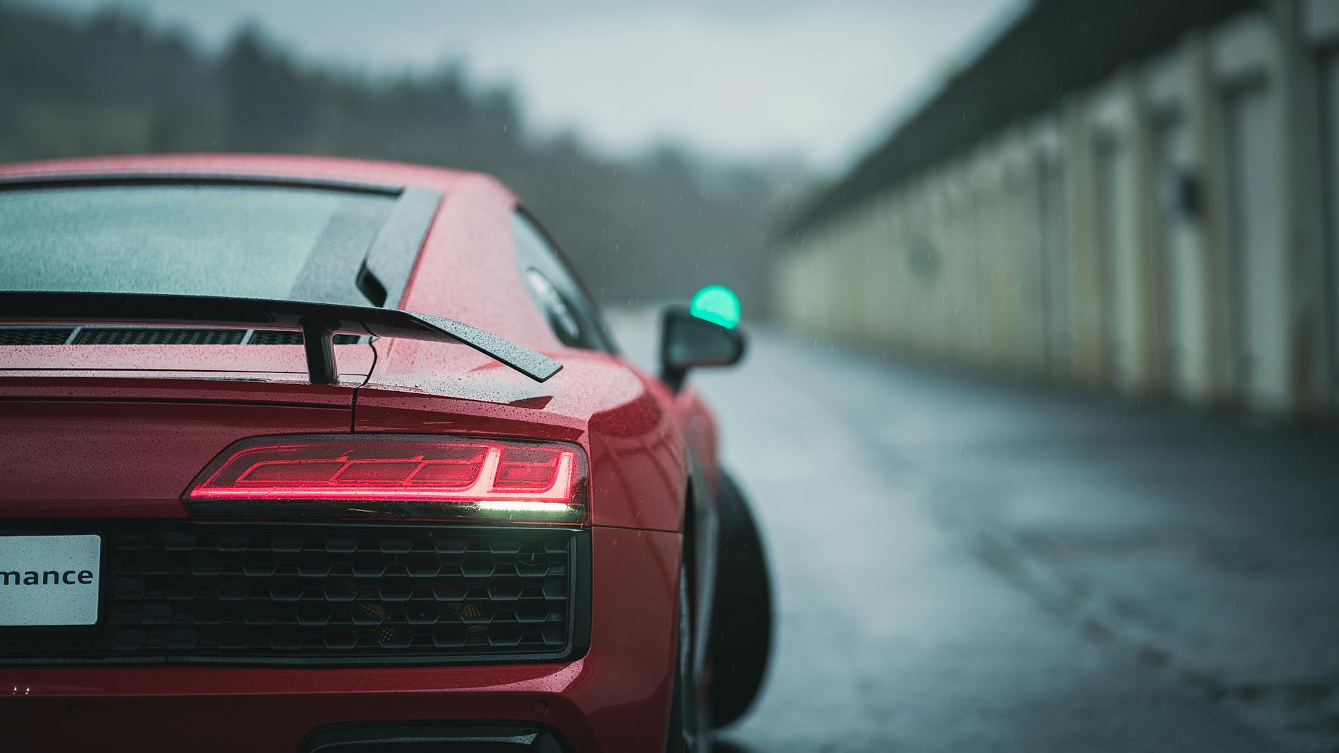 Rear view of a red sports car on a wet road, highlighting its sleek design and taillights.