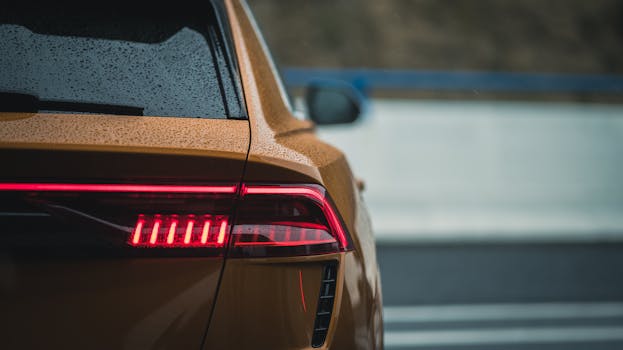 Detailed view of an illuminated red tail light on a yellow car during rainy conditions.