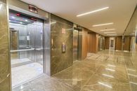 Interior of empty hallway with marble till in wall and floor with opened metal doors of elevator in multistory building