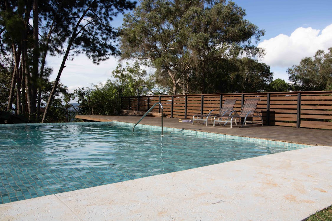 Free Swimming pool with clean transparent rippling water with deckchairs near fence in surrounded by green pants at tropical resort Stock Photo