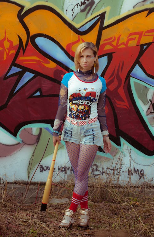 Young informal woman with baseball bat standing against vandalized wall