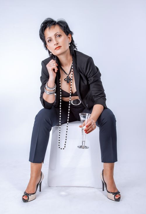 Free Fashionable woman in a black blazer sitting with elegance, holding a wine glass. Stock Photo