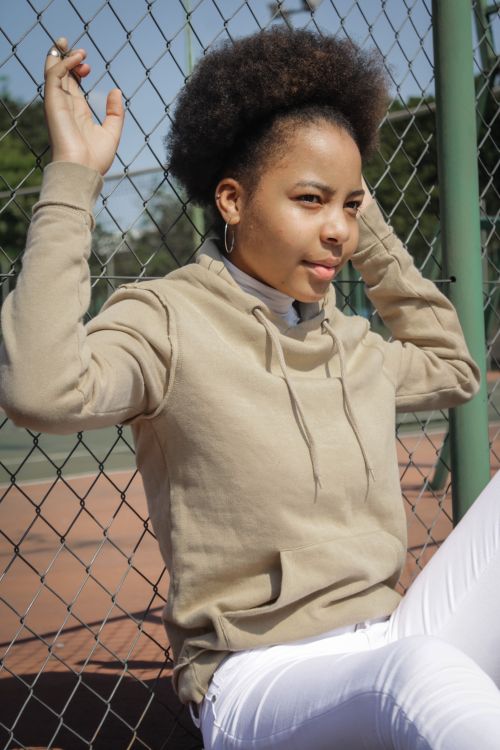 Free Outdoor portrait of young woman with afro hair leaning against a chain link fence. Stock Photo