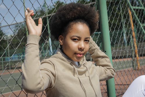 Free Girl in Beige Hoodie Sitting Against a Wire Fence Stock Photo