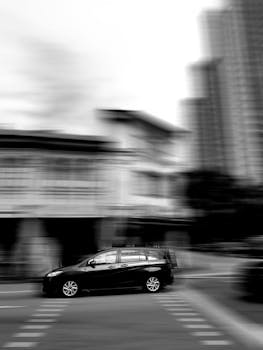 Black car in motion blur against a city backdrop in Singapore, grayscale tones.