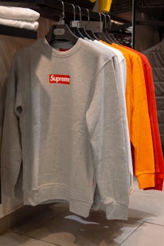 A selection of Supreme sweaters in various colors displayed on hangers inside a trendy clothing store.