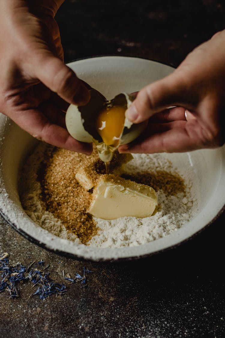 A Person Cracking An Egg In The Bowl