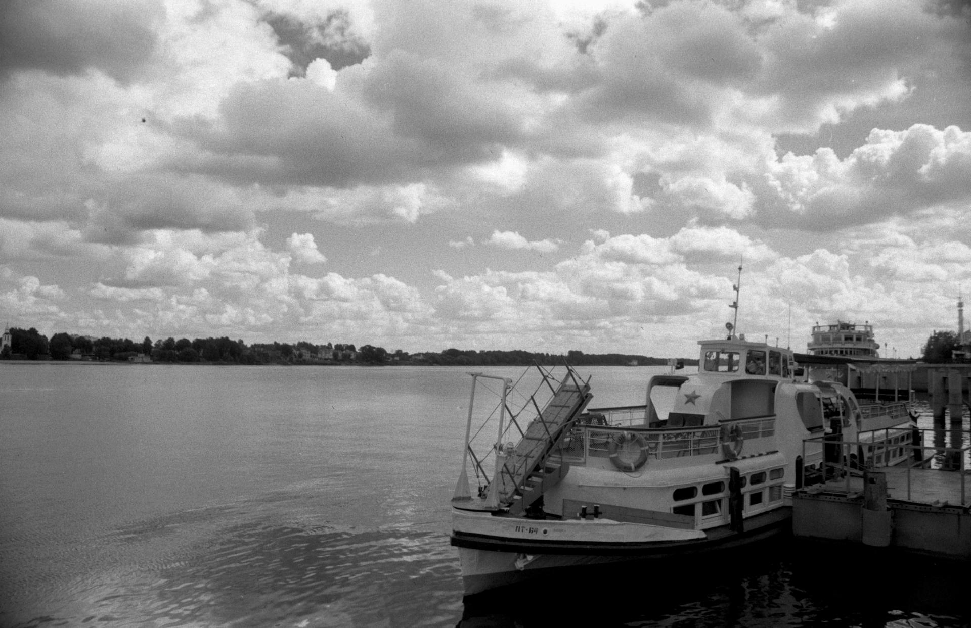 Black and white image of a ferry docked under a dramatic cloudy sky.