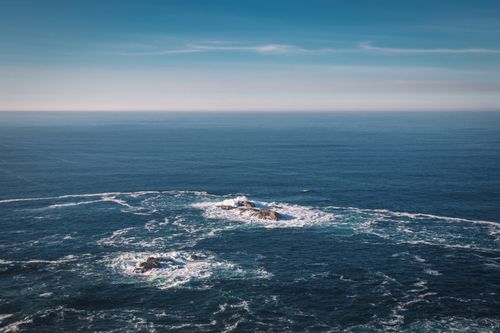 Free Aerial shot of the ocean with visible rock formations under a clear blue sky. Stock Photo