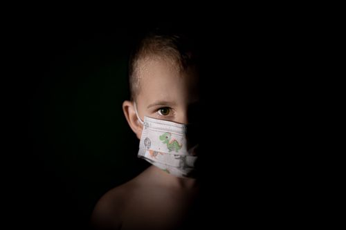 Free A young child in a face mask, partially lit against a dark background, symbolizing pandemic awareness. Stock Photo