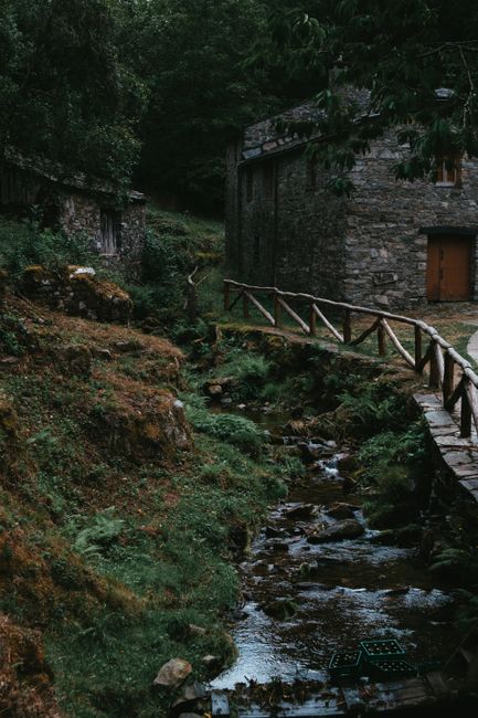 Peaceful rural landscape with a stream, wooden fence, and stone building in lush greenery.