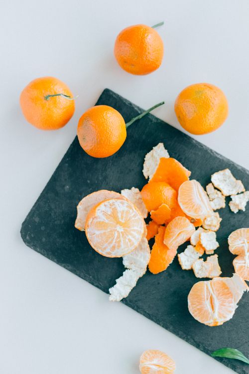 Free A high-angle shot of peeled mandarin oranges on a black chopping board, on a white surface. Stock Photo