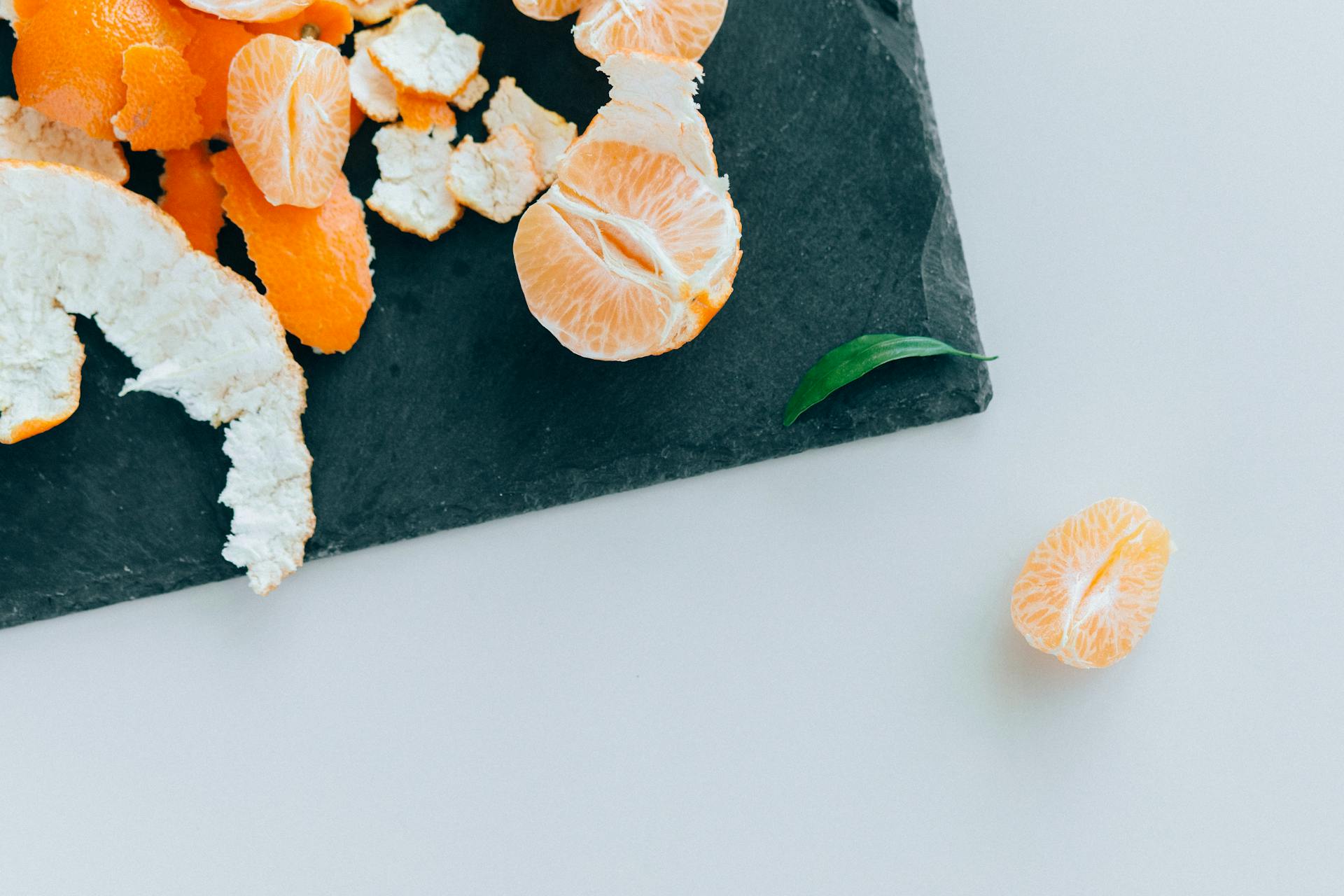 Top view of fresh mandarin slices and peel on a slate plate, highlighting healthy eating.