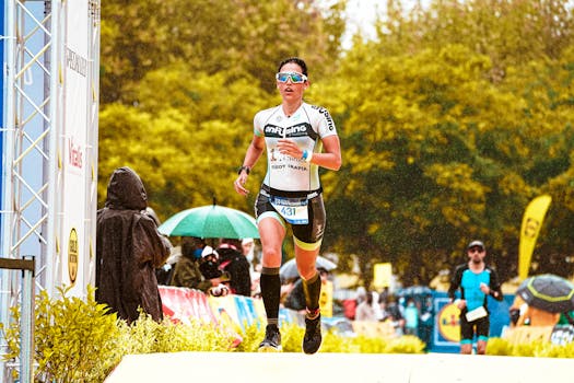 Female athlete competing in a rainy marathon under vibrant green trees during daylight.