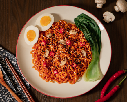 A vibrant plate of spicy noodles with boiled egg, mushrooms, and fresh greens.