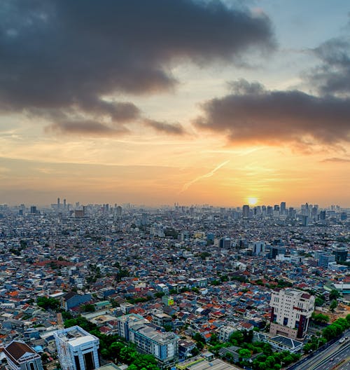 Aerial view of contemporary megapolis with different small and multistory buildings and skyscrapers against cloudy sunset sky