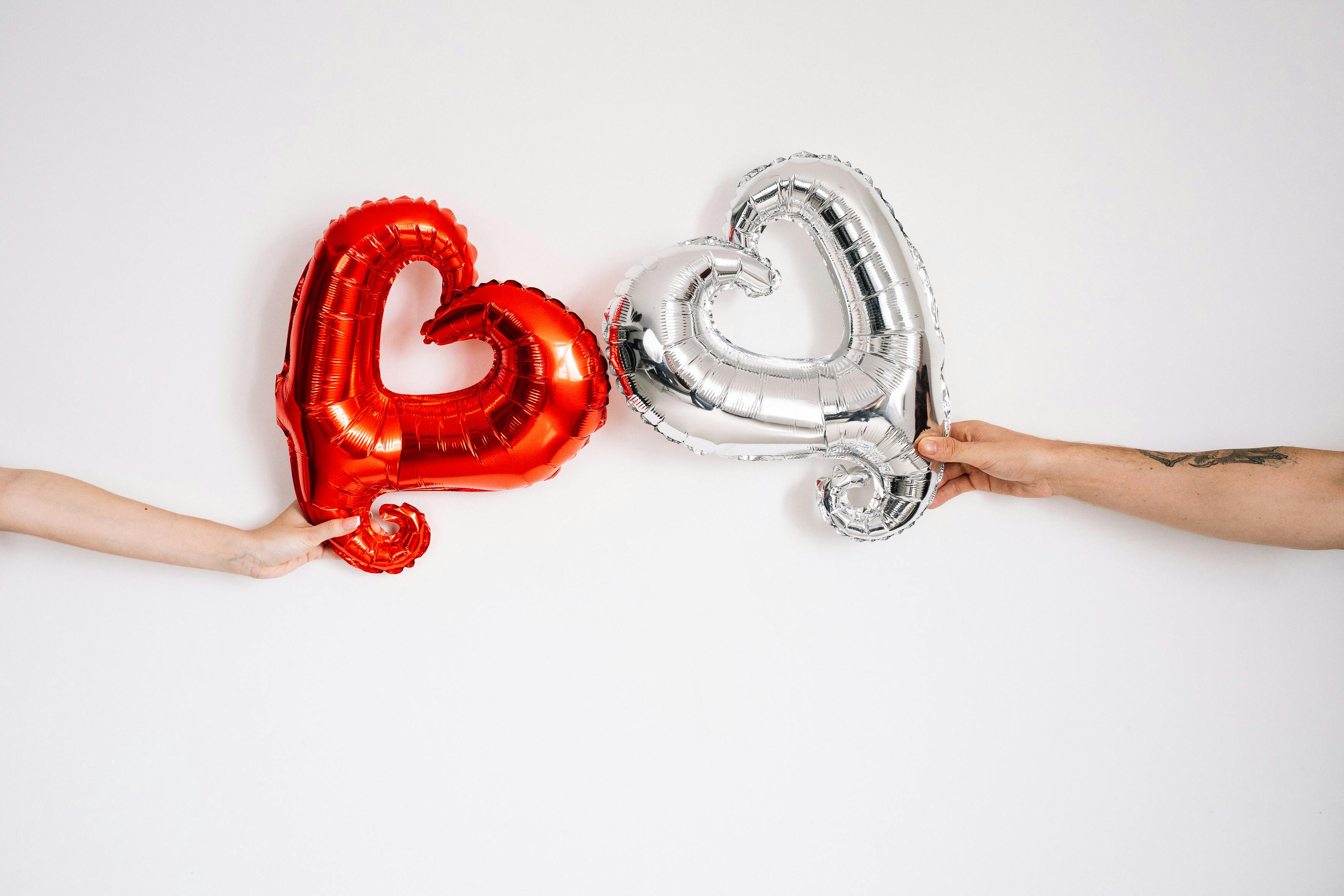 hands holding silver and red heart shaped balloons
