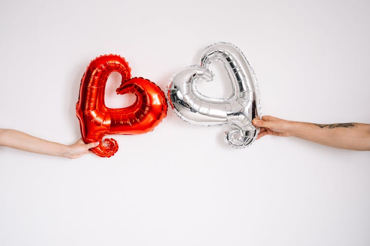 Hands Holding Silver And Red Heart Shaped Balloons