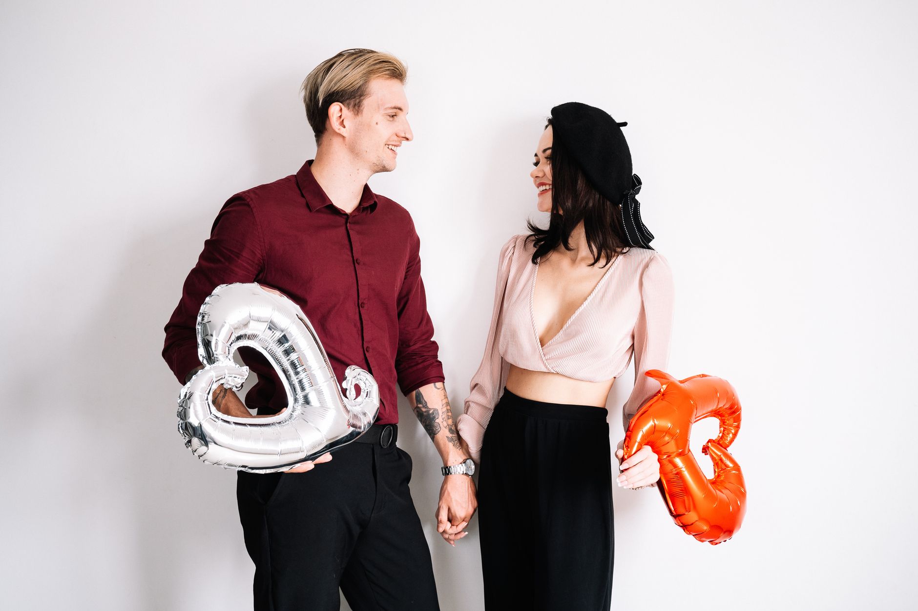 A happy young couple holding heart balloons and looking at each other in a studio setting.