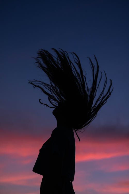 Woman with flipping hair standing against bright sunset